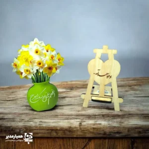 «او خواهد آمد»؛ جمله‌ای سرشار از امید و انتظار، با تصویر گل‌های دوست‌داشتنی نرگس و گلدان زرد، که به‌زیبایی روی این استند چوبی حک شده است. این استند چوبی می‌تواند مظهر دعا و آرزوی ظهور باشد؛ نمادی ساده و شیک برای تزئین اتاق، میز کار یا حتی قفسه کتابخانه. گل‌های نرگس در فرهنگ ایرانی یادآور انتظار و امید هستند و وجود این استند در خانه شما، حس مثبت و آرامش‌بخشی را منتقل می‌کند. ویژگی‌ها: ابعاد استاندارد و مناسب برای نمایش روی میز طرح چاپی با گل‌های نرگس و نوشته «او خواهد آمد» ساخته شده از چوب مرغوب و سبک هدیه‌ای معنوی، آرامش‌بخش و نمادین مناسب استفاده در مراسم مذهبی، جشن نیمه شعبان و یادبودها