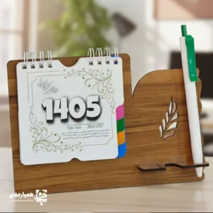"📆 تقویم رومیزی کد 102 | انتخابی شیک برای میزهای حرفه‌ای تقویم رومیزی کد 101 با طراحی چوبی و ساختار جمع‌وجور، گزینه‌ای بسیار کاربردی برای میز کار در محیط‌های اداری، آموزشی و سازمانی است. این محصول با ظاهر گرم چوب و طراحی مینیمال، همزمان حس نظم، زیبایی و حرفه‌ای بودن را به میز شما می‌بخشد. بدنه این تقویم از MDF دورو با کیفیت بالا ساخته شده و ابعاد پایه آن 18*13 سانتی‌متر است که فضای کمی اشغال کرده و برای هر نوع میز کاری مناسب می‌باشد. برگه‌های تقویم با ابعاد 10.7×9.6 سانتی‌متر از کاغذ گلاسه 200 گرم تهیه شده‌اند که علاوه بر خوانایی بالا، از دوام و ماندگاری مناسبی برخوردار هستند. صحافی فنری، ورق‌زدن آسان و استفاده روزمره را بسیار راحت کرده است. ⭐ تقویم رومیزی کد 101 در رنگ‌بندی متنوع (گردو جنگلی،فندقی،گردویی تیره) تولید می‌شود تا با سلیقه‌ها و دکوراسیون‌های مختلف هماهنگ باشد. مهم‌ترین مزیت این محصول، قابلیت شخصی‌سازی اختصاصی آن است؛ امکان درج نام، لوگو یا اطلاعات سازمان، مدرسه یا برند این تقویم را به یک هدیه تبلیغاتی ماندگار و مؤثر تبدیل می‌کند. کد محصول: 101 جنس بدنه: MDF دورو ابعاد پایه: 18*13 سانتی‌متر ابعاد برگه: 10.7×9.6 سانتی‌متر کاغذ: گلاسه 200 گرم قابلیت شخصی‌سازی اختصاصی تقویم رومیزی کد 102؛ انتخابی هوشمندانه برای میز کار، هدیه سازمانی و تبلیغات ماندگار ✅ "
