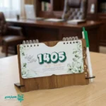 "📆 تقویم رومیزی کد 201 | انتخابی شیک برای میزهای حرفه‌ای تقویم رومیزی کد 105 با طراحی چوبی و ساختار جمع‌وجور، گزینه‌ای بسیار کاربردی برای میز کار در محیط‌های اداری، آموزشی و سازمانی است. این محصول با ظاهر گرم چوب و طراحی مینیمال، همزمان حس نظم، زیبایی و حرفه‌ای بودن را به میز شما می‌بخشد. بدنه این تقویم از MDF دورو با کیفیت بالا ساخته شده و ابعاد پایه آن 18*12 سانتی‌متر است که فضای کمی اشغال کرده و برای هر نوع میز کاری مناسب می‌باشد. برگه‌های تقویم با ابعاد 8.5*16 سانتی‌متر از کاغذ گلاسه 200 گرم تهیه شده‌اند که علاوه بر خوانایی بالا، از دوام و ماندگاری مناسبی برخوردار هستند. صحافی فنری، ورق‌زدن آسان و استفاده روزمره را بسیار راحت کرده است. ⭐ تقویم رومیزی کد 104 در رنگ‌ (جنگلی ،فندوقی،گردویی تیره ) تولید می‌شود تا با سلیقه‌ها و دکوراسیون‌های مختلف هماهنگ باشد. مهم‌ترین مزیت این محصول، قابلیت شخصی‌سازی اختصاصی آن است؛ امکان درج نام، لوگو یا اطلاعات سازمان، مدرسه یا برند این تقویم را به یک هدیه تبلیغاتی ماندگار و مؤثر تبدیل می‌کند. کد محصول: 201 جنس بدنه: MDF دورو ابعاد پایه18*12 سانتی‌متر ابعاد برگه:16*8.5سانتی‌متر کاغذ: گلاسه 200 گرم قابلیت شخصی‌سازی اختصاصی تقویم رومیزی کد 105؛ انتخابی هوشمندانه برای میز کار، هدیه سازمانی و تبلیغات ماندگار ✅ "