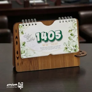 "📆 تقویم رومیزی کد 202 | انتخابی شیک برای میزهای حرفه‌ای تقویم رومیزی کد 202 با طراحی چوبی و ساختار جمع‌وجور، گزینه‌ای بسیار کاربردی برای میز کار در محیط‌های اداری، آموزشی و سازمانی است. این محصول با ظاهر گرم چوب و طراحی مینیمال، همزمان حس نظم، زیبایی و حرفه‌ای بودن را به میز شما می‌بخشد. بدنه این تقویم از MDF دورو با کیفیت بالا ساخته شده و ابعاد پایه آن 13*20 سانتی‌متر است که فضای کمی اشغال کرده و برای هر نوع میز کاری مناسب می‌باشد. برگه‌های تقویم با ابعاد 8.5*16 سانتی‌متر از کاغذ گلاسه 200 گرم تهیه شده‌اند که علاوه بر خوانایی بالا، از دوام و ماندگاری مناسبی برخوردار هستند. صحافی فنری، ورق‌زدن آسان و استفاده روزمره را بسیار راحت کرده است. ⭐ تقویم رومیزی کد 202 در رنگ‌3 رنگ متنوع (گردوجنگلی ،فندوقی،گردویی تیره ) تولید می‌شود تا با سلیقه‌ها و دکوراسیون‌های مختلف هماهنگ باشد. مهم‌ترین مزیت این محصول، قابلیت شخصی‌سازی اختصاصی آن است؛ امکان درج نام، لوگو یا اطلاعات سازمان، مدرسه یا برند این تقویم را به یک هدیه تبلیغاتی ماندگار و مؤثر تبدیل می‌کند. کد محصول: 202 جنس بدنه: MDF دورو ابعاد پایه13*20 سانتی‌متر ابعاد برگه:16*8.5سانتی‌متر کاغذ: گلاسه 200 گرم قابلیت شخصی‌سازی اختصاصی تقویم رومیزی کد 202؛ انتخابی هوشمندانه برای میز کار، هدیه سازمانی و تبلیغات ماندگار ✅ "