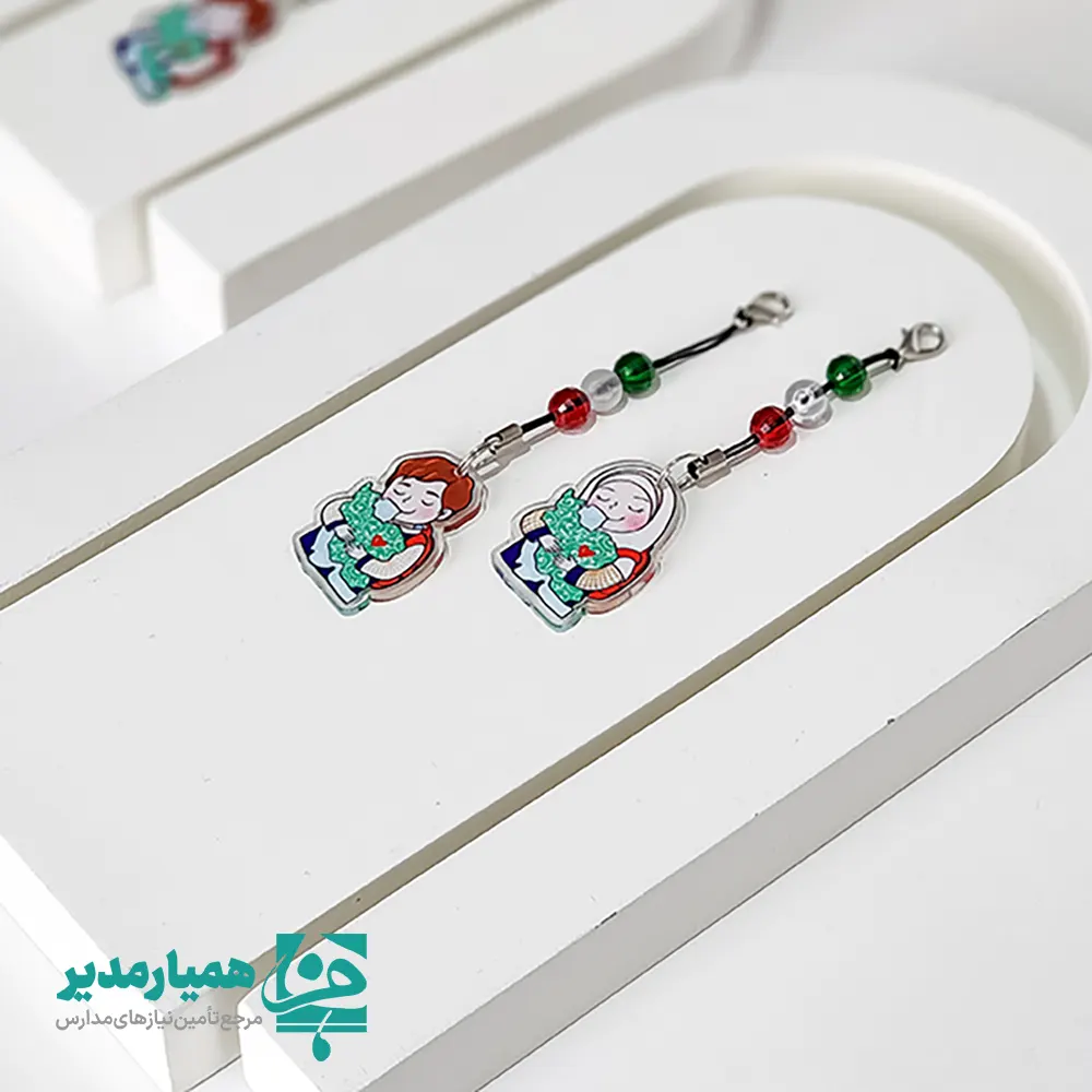 🇮🇷✨ آویز ایران من یکی از محصولات خاص و ارزشمند همیار مدیر است که با الهام از مفاهیم ملی، میهن‌دوستی و هویت ایرانی، برای مناسبت‌های مهمی همچون دهه فجر انقلاب اسلامی و روز دانش‌آموز طراحی شده است. این محصول از جنس پلکسی ساخته شده و با ابعاد ۳.۵ سانتی‌متر و وزن بسیار سبک حدود ۵ گرم، گزینه‌ای مناسب برای استفاده روزمره کودکان و نوجوانان می‌باشد. 🎨❤️ طراحی این آویز شامل آویز تصویری از دختر و پسر است که کشور ایران را در آغوش گرفته‌اند؛ نمادی زیبا از عشق به میهن و همبستگی ملی. در قسمت بالای آویز نیز سه مهره به ترتیب رنگ‌های پرچم ایران 🚩 قرار گرفته که جلوه‌ای خاص و چشم‌نواز به محصول بخشیده است. 🎁✨ این آوثیز پلکسی می‌تواند به عنوان یک گیفت فرهنگی ماندگار در مدارس، مساجد و مؤسسات فرهنگی مورد استفاده قرار گیرد و انتخابی مناسب برای هدیه دادن به دانش‌آموزان در برنامه‌ها و جشن‌های مناسبتی باشد.