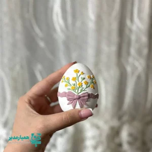 🌸 تخم‌مرغ تزئینی نوروزی، یکی از محصولات هنری و خاص مجموعه کیمیا هنر است که با الهام از آیین‌های کهن نوروز و نمادهای اصیل بهاری طراحی شده است. این محصول از سنگ مصنوعی با کیفیت بالا ساخته شده و با ابعاد حدود ۶.۵ سانتی‌متر و وزن تقریبی 30 گرم، گزینه‌ای سبک، خوش‌دست و در عین حال ماندگار برای هدیه محسوب می‌شود. 🌷 سطح این تخم‌مرغ‌های تزئینی با نمادهای برجسته مخصوص نوروز تزئین شده است؛ از گل‌های بهاری گرفته تا سمبل های نوروزی مانند شکوفه‌ها، شاخه‌های سبز، پرندگان، طرح‌های سنتی الهام‌گرفته از هفت‌سین. این تنوع در طراحی باعث شده هر محصول جلوه‌ای متفاوت و منحصر‌به‌فرد داشته باشد. 🌼 ترکیب فرم نمادین تخم‌مرغ نوروزی با استیکرهای برجسته و رنگ‌آمیزی ظریف، این گیفت را به انتخابی خاص برای گیفت نوروزی، هدایای فرهنگی و یادبودهای مناسبتی تبدیل کرده است. این محصول حس تازگی، شروع دوباره و طراوت بهار را به‌خوبی منتقل می‌کند و برای مخاطبان مختلف جذابیت دارد. 🌺 تخم‌مرغ تزئینی نوروزی کیمیا هنر گزینه‌ای مناسب برای استفاده در مدارس، مراکز فرهنگی، مؤسسات آموزشی، سازمان‌ها و شرکت‌هاست و می‌تواند به‌عنوان هدیه نوروزی سازمانی، یادبود مراسم‌ها و یا هدیه‌ای صمیمی برای کارکنان و مخاطبان مورد استفاده قرار گیرد. 🌸 استفاده از سنگ مصنوعی با کیفیت، دوام و ماندگاری بالای محصول را تضمین می‌کند تا این گیفت نوروزی برای سال‌ها به‌عنوان یادگاری از نوروز باقی بماند. وزن کم و ابعاد استاندارد آن نیز حمل، بسته‌بندی و توزیع را بسیار آسان کرده است. 🌷 این تخم‌مرغ‌های تزئینی در طرح‌ها و رنگ‌بندی‌ها ی متنوع نوروزی تولید می‌شوند و امکان انتخاب یا سفارش متناسب با سلیقه شخصی یا هویت بصری سازمان‌ها را فراهم می‌کنند. اگر به دنبال هدیه‌ای متفاوت، هنری و ریشه‌دار در فرهنگ ایرانی هستید، این محصول انتخابی هوشمندانه و ماندگار خواهد بود.