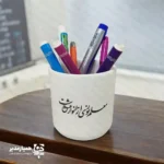 🌟 اگر به دنبال یک هدیه هم‌زمان زیبا، کاربردی و فرهنگی برای روز معلم هستید، جاقلمی سفالی طرح روز معلم می‌تواند انتخابی بسیار مناسب برای شما باشد. این جاقلمی با جنس سفالی باکیفیت تولید شده و با ارتفاع حدود ۱۱ سانتی‌متر و وزن تقریبی ۱۳۰ گرم، ابعادی کاملاً استاندارد برای قرار دادن روی میز کار، میز کلاس یا میز مطالعه دارد. روی بدنه این جاقلمی، چاپ برجسته با طرح‌های مرتبط با معلم و پیام‌های تقدیرآمیز کار شده که جلوه‌ای چشم‌نواز و ماندگار ایجاد می‌کند. این محصول در دو مدل متفاوت عرضه می‌شود: مدل‌های مناسب سلیقه‌های رسمی‌تر و مدل‌هایی با حال‌وهوای شاد و دوستانه برای مدارس و دانش‌آموزان. ✏️📚 این جاقلمی گزینه‌ای عالی برای موارد زیر است: هدیه روز معلم از طرف دانش‌آموزان یا اولیا 👩‍🏫💐 پک‌های فرهنگی و هدایای رسمی مدارس و آموزشگاه‌ها تقدیر از معلمان در مراسم پایان سال تحصیلی و جشن‌های مناسبتی استفاده روی میز کار معلم، مدیر یا کادر آموزشی ترکیب طراحی ساده و شیک، چاپ برجسته و کاربرد روزمره، جاقلمی سفالی روز معلم را به یادگاری‌ای تبدیل کرده که هر روز مقابل چشم معلم خواهد بود و او را به یاد محبت و توجه شما می‌اندازد. 🌷 این محصول می‌تواند به تنهایی یا همراه با سایر هدایای فرهنگی، در بسته‌های هدیه مدارس و موسسات آموزشی قرار گیرد.