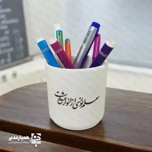 🌟 اگر به دنبال یک هدیه هم‌زمان زیبا، کاربردی و فرهنگی برای روز معلم هستید، جاقلمی سفالی طرح روز معلم می‌تواند انتخابی بسیار مناسب برای شما باشد. این جاقلمی با جنس سفالی باکیفیت تولید شده و با ارتفاع حدود ۱۱ سانتی‌متر و وزن تقریبی ۱۳۰ گرم، ابعادی کاملاً استاندارد برای قرار دادن روی میز کار، میز کلاس یا میز مطالعه دارد. روی بدنه این جاقلمی، چاپ برجسته با طرح‌های مرتبط با معلم و پیام‌های تقدیرآمیز کار شده که جلوه‌ای چشم‌نواز و ماندگار ایجاد می‌کند. این محصول در دو مدل متفاوت عرضه می‌شود: مدل‌های مناسب سلیقه‌های رسمی‌تر و مدل‌هایی با حال‌وهوای شاد و دوستانه برای مدارس و دانش‌آموزان. ✏️📚 این جاقلمی گزینه‌ای عالی برای موارد زیر است: هدیه روز معلم از طرف دانش‌آموزان یا اولیا 👩‍🏫💐 پک‌های فرهنگی و هدایای رسمی مدارس و آموزشگاه‌ها تقدیر از معلمان در مراسم پایان سال تحصیلی و جشن‌های مناسبتی استفاده روی میز کار معلم، مدیر یا کادر آموزشی ترکیب طراحی ساده و شیک، چاپ برجسته و کاربرد روزمره، جاقلمی سفالی روز معلم را به یادگاری‌ای تبدیل کرده که هر روز مقابل چشم معلم خواهد بود و او را به یاد محبت و توجه شما می‌اندازد. 🌷 این محصول می‌تواند به تنهایی یا همراه با سایر هدایای فرهنگی، در بسته‌های هدیه مدارس و موسسات آموزشی قرار گیرد.