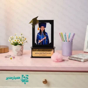 🎓🌟 تندیس فارغ‌التحصیلی قاب عکس – یادگاری باشکوه از لحظه‌های موفقیت تحصیلی ✨📚 تندیس فارغ‌التحصیلی قاب عکس، هدیه‌ای خاص و ماندگار برای ثبت خاطرات شیرین پایان سال تحصیلی است 💛🎉. طراحی این محصول بدون چاپ عکس انجام شده تا امکان قرار دادن تصویر دانش‌آموز در ابعاد 📸 ۱۰×۱۵ سانتی‌متر فراهم باشد. وجود عنصر نمادین 🎓 کلاه فارغ‌التحصیلی در بالای قاب، حس افتخار و موفقیت تحصیلی را زیبایی خاصی می‌بخشد 🌈👏. جنس این تندیس از چوب باکیفیت 🪵 بوده و با وزن سبک حدود ⚖️ ۵۵ گرم، انتخابی ایده‌آل برای قرار دادن روی میز، شلف یا ویترین محسوب می‌شود 💫. تلفیق شیک طراحی کلاسیک با جزئیات لطیف کودکانه، آن را به گزینه‌ای مناسب برای فضای آموزشی و فرهنگی تبدیل کرده است 🏫💖. این تندیس پیشنهاد ویژه‌ای برای 🎈 جشن الفبا و 🎉 فارغ‌التحصیلی مقاطع پیش‌دبستان و ابتدایی است تا خاطرات نخستین موفقیت‌های تحصیلی کودکان را جاودانه سازد 🧸🌟. محصولی زیبا، کاربردی و پرطرفدار برای مدارس، آموزشگاه‌ها و مراکز فرهنگی جهت تقدیر از تلاش‌های کوچک ولی پرافتخار کودکان 💐🎁.