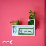  تابلو ی چوبی سر در حس خوب ؛ ترکیب زیبایی و نظم در فضای اداری تابلو چوبی سر در حس خوب راهکاری حرفه‌ای برای نظم‌دهی و زیباسازی فضاهای اداری و آموزشی است. این تابلو با طراحی مدرن  علاوه بر معرفی اتاق‌ها، جلوه‌ای شیک و منظم به محیط کار شما می‌بخشد. استفاده از متریال  پلکسی گلاس در ساخت این محصول باعث شده تا در برابر گردوغبار، رطوبت و ضربه مقاومت بالایی داشته باشد. بنابراین این تابلو گزینه‌ای مناسب برای نصب در مدارس، شرکت‌ها، سازمان‌ها و موسسات آموزشی محسوب می‌شود. ویژگی‌های اصلی محصول ساخته شده از پلکسی گلاس باکیفیت طراحی مدرن و جذاب مناسب محیط‌های اداری و آموزشی مقاوم در برابر گردوغبار و ضربه نصب آسان روی دیوار یا درب اتاق مناسب برای معرفی اتاق مدیریت، کلاس‌ها و بخش‌های مختلف سازمان همراه با گلدان(بدون گل) و پرنده سفالی امکان سفارشی‌سازی یکی از مهم‌ترین مزایای این محصول، امکان طراحی اختصاصی است. شما می‌توانید نام اتاق، لوگوی مجموعه یا هر متن دلخواه را روی تابلو درج کنید تا هویت بصری سازمان شما به شکلی حرفه‌ای نمایش داده شود. این تابلو گزینه‌ای ایده‌آل برای مدارس، شرکت‌ها، دفاتر اداری و موسسات آموزشی است و به مراجعه‌کنندگان کمک می‌کند مسیر خود را سریع‌تر پیدا کنند، در حالی که ظاهر محیط نیز مرتب و حرفه‌ای باقی می‌ماند.